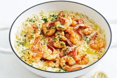 a white bowl filled with rice and shrimp on top of a table next to a lemon wedge