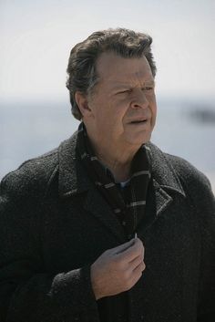 a man with his eyes closed standing by the water looking off into the distance while wearing a coat and scarf