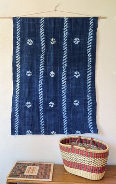 a basket sitting on top of a wooden table next to a blue and white wall hanging