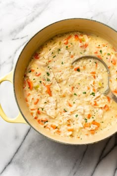 a pot filled with chicken and rice soup on top of a marble countertop next to a wooden spoon