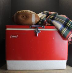 an old fashioned ice chest with a football and plaid blanket on it's top