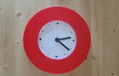 a red and white clock on a wooden surface