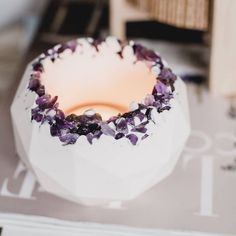 a white vase filled with purple flowers sitting on top of a table next to a book