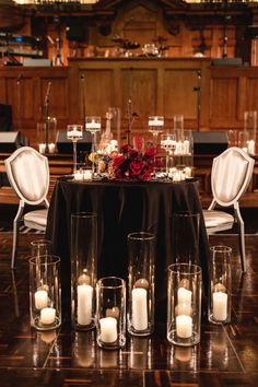 a table topped with lots of candles and vases filled with flowers on top of a wooden floor