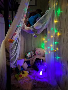 a teddy bear sitting in a hammock with lights around it and books on the floor