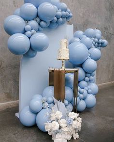 a cake on a table surrounded by blue balloons and white flowers in front of it