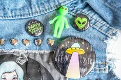 some pins are laying on the back of someone's jean pants and there is an alien pin