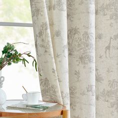 a table with a cup and saucer on it next to a window covered in curtains