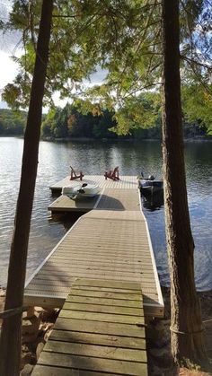 two boats are docked at the end of a dock in front of some trees and water