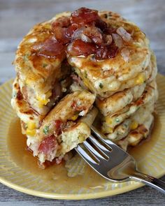 stack of pancakes with bacon and cheese on yellow plate next to fork, closeup