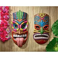 three masks are hanging on the wall next to some pink and green flowers in front of them