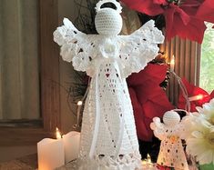 a crocheted angel ornament sitting on top of a table next to candles