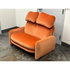 an orange reclining chair sitting in front of a white wall with a door behind it