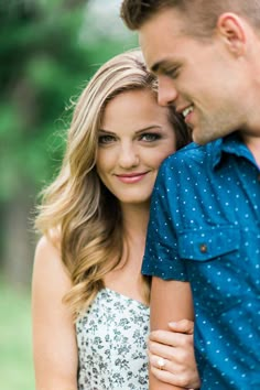 a man and woman standing next to each other with their arms around each other in front of trees