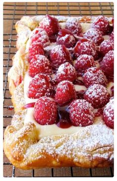 a pastry covered in powdered sugar and raspberries on a wire cooling rack