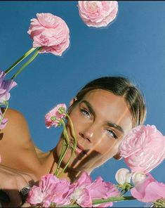 a woman is surrounded by pink flowers in the air with her face partially obscured by blue sky