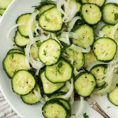 a white plate topped with cucumbers and onions next to a fork on top of a table