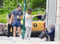 a man and woman standing on the sidewalk next to a yellow taxi