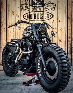 a black motorcycle parked next to a wooden wall with the words moto design customs on it