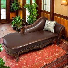 a brown leather chaise lounge sitting on top of a rug next to potted plants