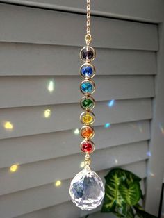 a multicolored glass bead hanging from a gold plated chain on a window sill