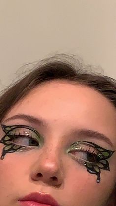 a woman with black and green makeup looks at the camera while wearing butterfly wings on her eyes