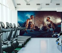 a gym with rows of exercise machines and large wall mural in the background that depicts two men working on their muscles