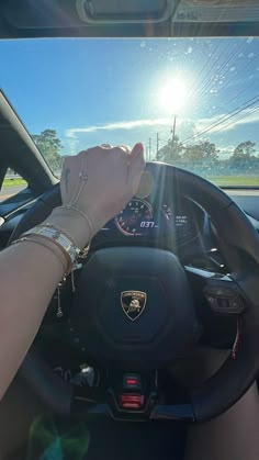 a woman driving a car with her hand on the steering wheel and sun shining in the background