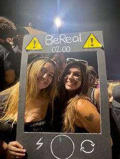 two women are posing for a photo in front of a sign that says be real