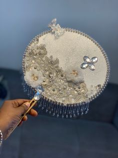 a person holding a decorative object with beads and pearls on it, in front of a blue couch