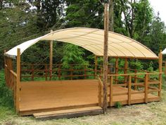 a wooden deck with an awning over it in the middle of some trees and grass