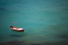 an orange and white boat floating on top of the ocean next to shore line with blue water