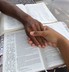 two people holding hands over an open book