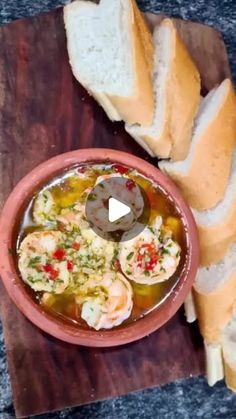 a bowl filled with soup next to sliced bread on top of a wooden cutting board