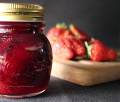 a jar filled with red liquid next to strawberries on a cutting board in the background