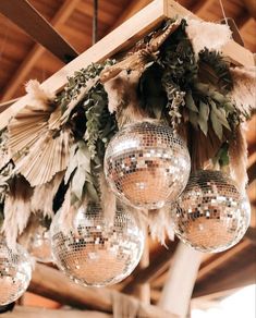 several disco balls hanging from the ceiling with greenery on them and some feathers attached to it