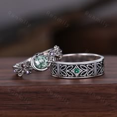 two silver rings with green stones on them sitting on a wooden table next to each other