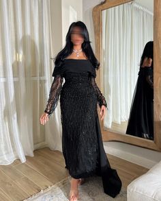 a woman standing in front of a mirror wearing a long black dress with sheer sleeves