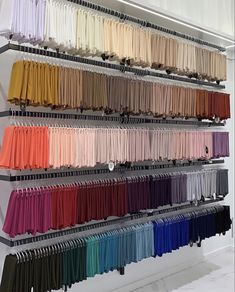 there is a rack with many colors of clothes hanging from it's hooks on the wall