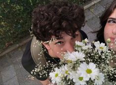 two young people are looking at the camera with flowers in front of their faces and behind them is a bouquet of daisies