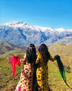 two women are sitting on a hill with mountains in the background