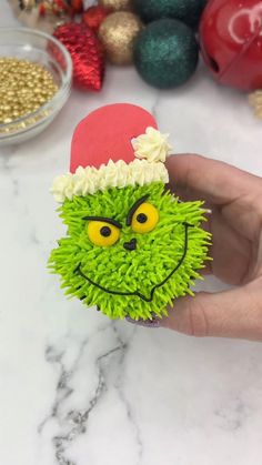 a hand holding a green cupcake with a grin face on it