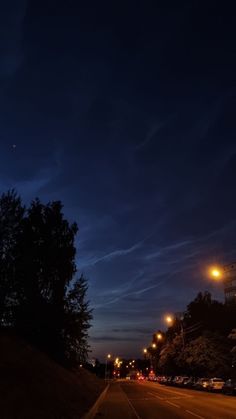 an empty street at night with cars parked on the side and trees in the background