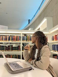 a woman sitting at a table with a laptop in front of her and bookshelves behind her