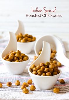 four white bowls filled with nuts sitting on top of a cloth covered table next to spoons