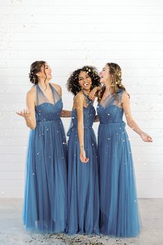 three women in blue dresses are laughing and posing for the camera with confetti falling all around them