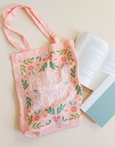 a pink bag sitting on top of a table next to an open book