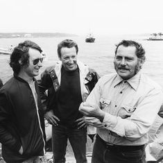 black and white photograph of three men standing on the deck of a boat, smiling