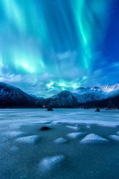 an aurora bore is seen above the snow covered mountains and ice - covered water in this photo