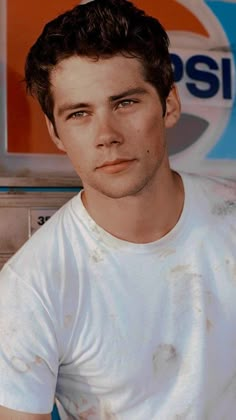 the young man is posing in front of a pepsi sign and wearing a white t - shirt